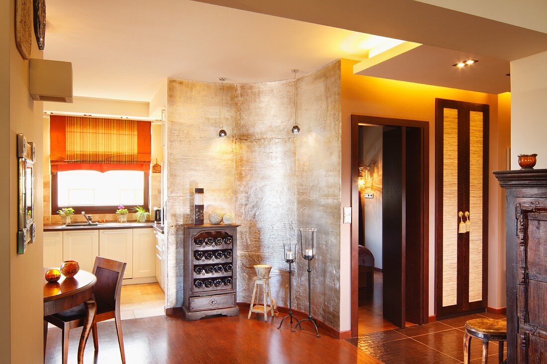 Silbern schimmernde, geschwungene Raumteilerwand mit Weinregal vor moderner Einbauküche, Essplatz mit Biedermeiertisch