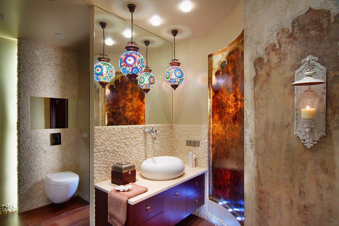 Colourful, patterned spherical lamps above washstand with pebble mosaic tiles, separate toilet and vintage Oriental-style wall design