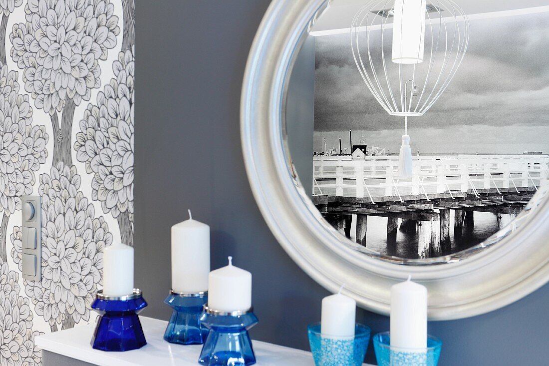 Photo mural depicting old wooden pier reflected in round mirror; blue glass candlesticks in foreground