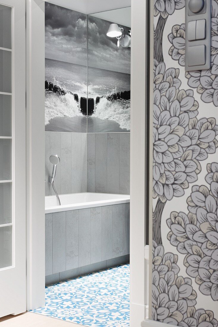 Blick durch offene Tür ins Badezimmer auf eine Übereck gespiegelte Fototapete mit Schwarz-Weiß-Abbildung von Meer und Himmel