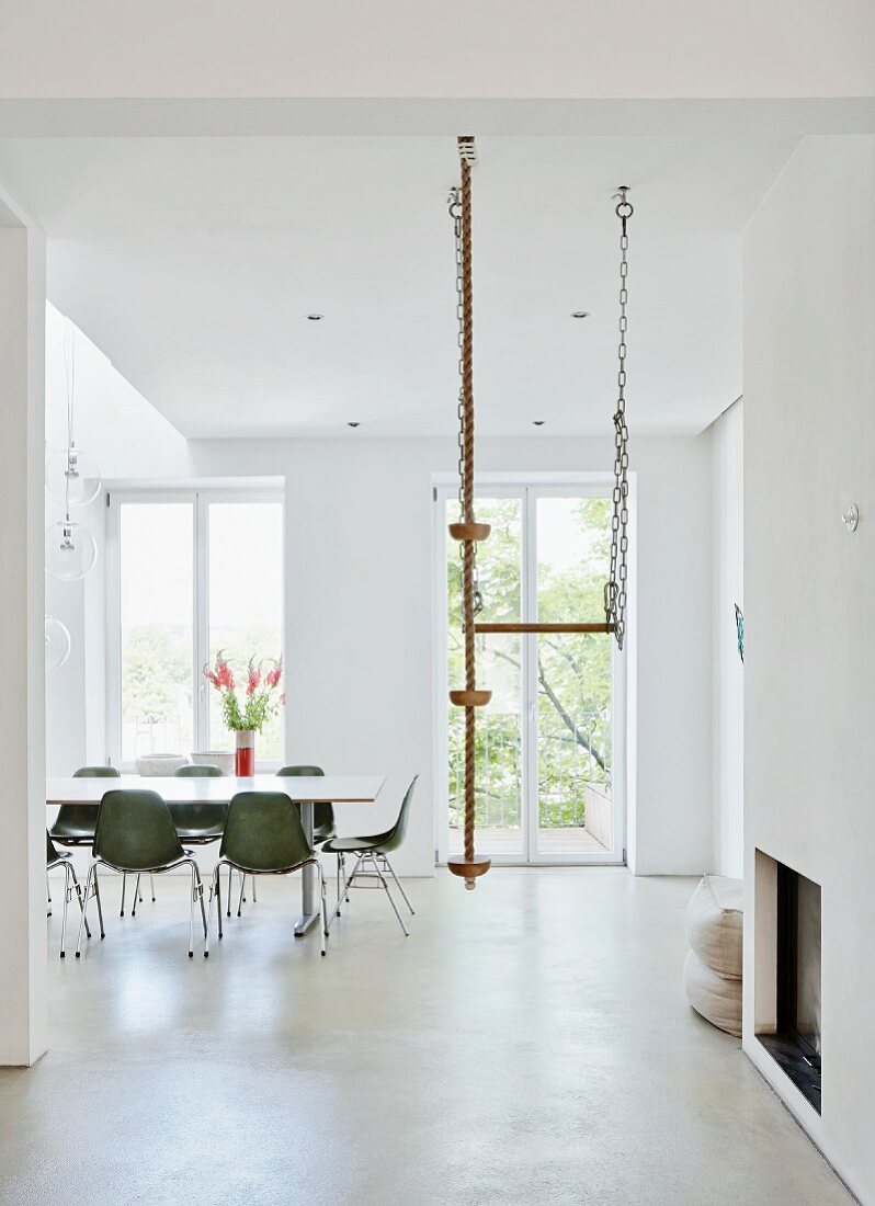 Green shell chairs and climbing rope hanging from ceiling in minimalist, white dining room