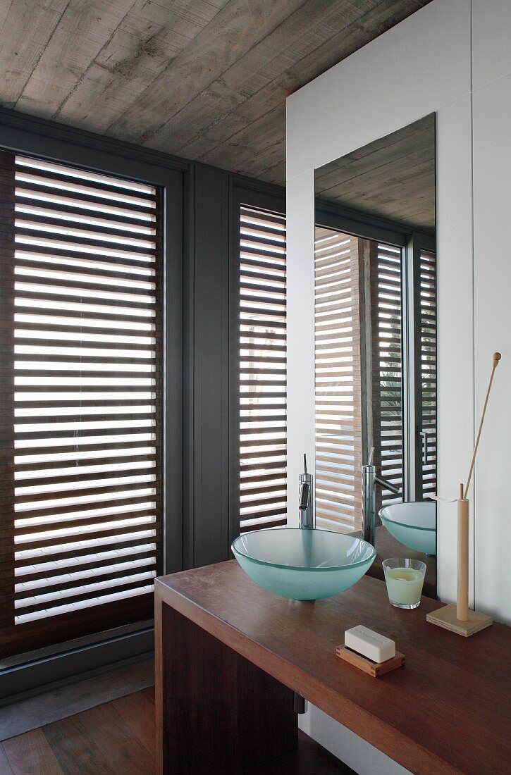 Waschbereich mit minimalistischem Waschtisch, Glasschüssel auf Holztisch, gegenüber Terrassentür mit geschlossenem Holzlamellen
