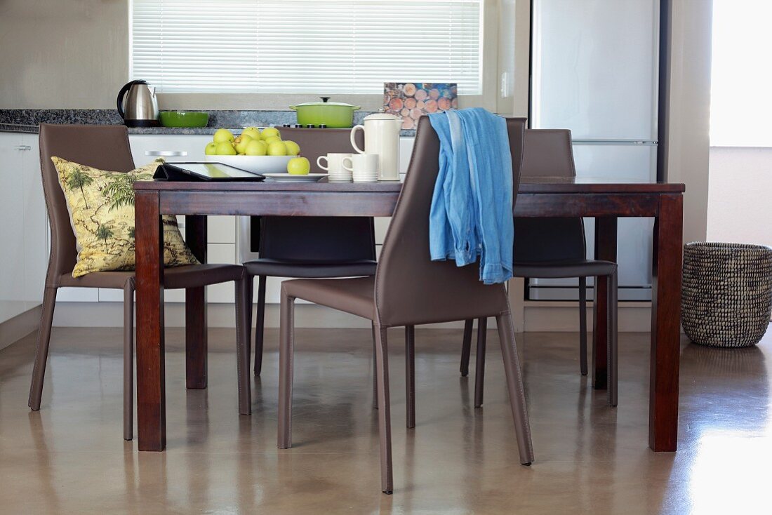 Dunkler Holzesstisch und graue Kunststoff Stühle auf poliertem Estrichboden