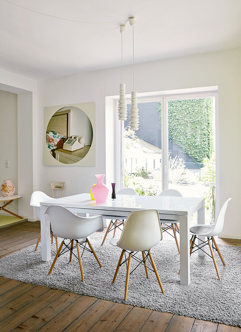 Classic chairs around white table below modern pendant lamps in front of French windows