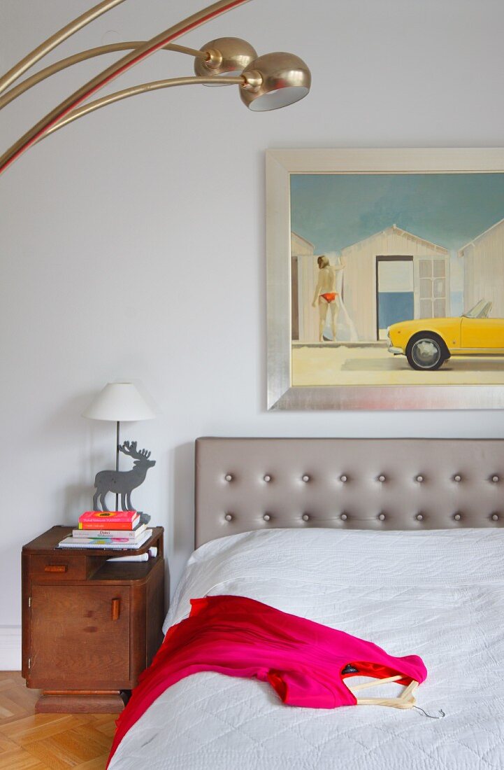 Pink dress on bed with grey upholstered headboard below framed modern artwork on wall