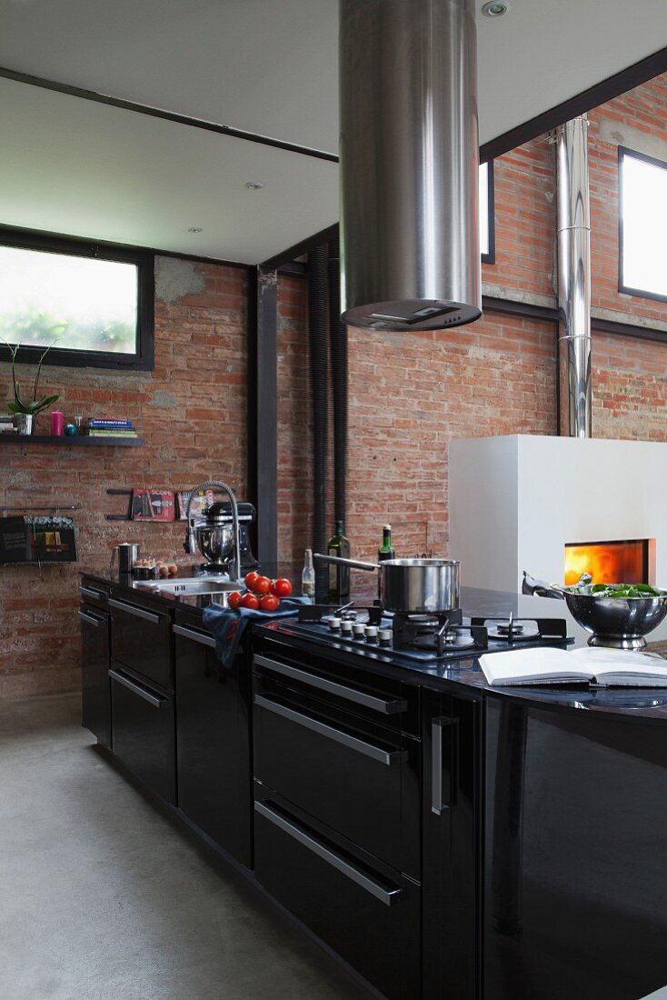 Black kitchen counter below cylindrical stainless steel extractor hood in front of brick wall