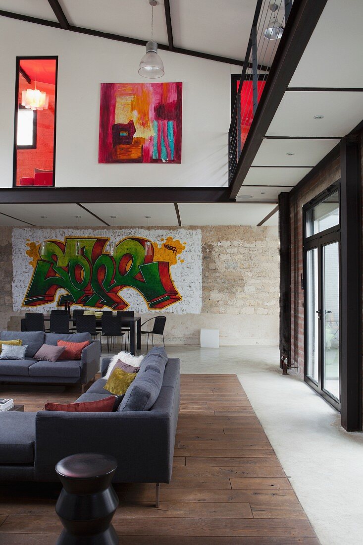 Loungebereich mit grauen Sofas, im Hintergrund Essplatz vor Wand mit Graffiti Bild in Loftwohnung mit umlaufender Galerie