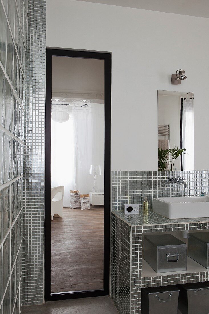 Bad mit Standspiegel neben Waschtisch mit silberfarbenen, glänzenden Mosaikfliesen