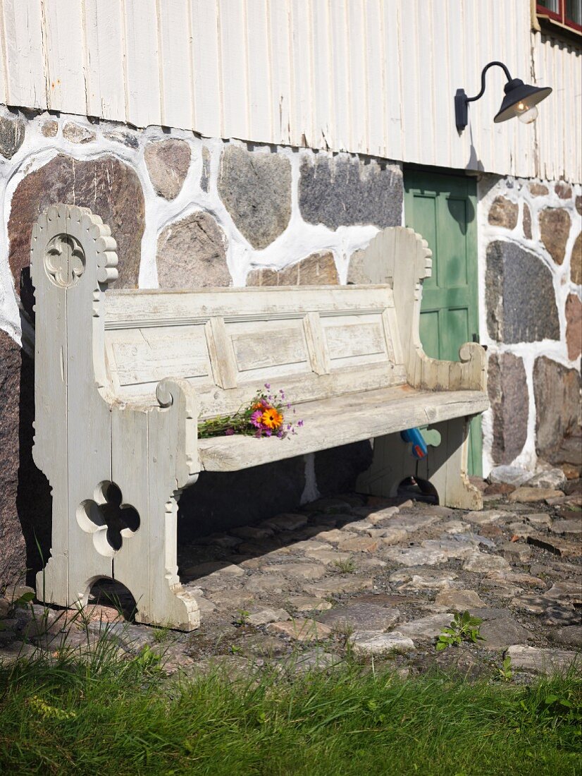 Carved, rustic-style, weathered wooden bench against stone wall base of country house