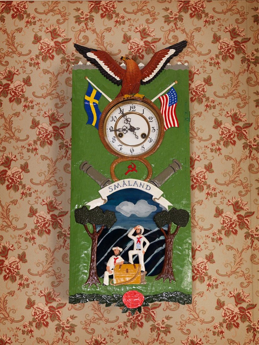 Clock with flag and eagle motifs on painted metal case hung on wall with vintage-style floral wallpaper