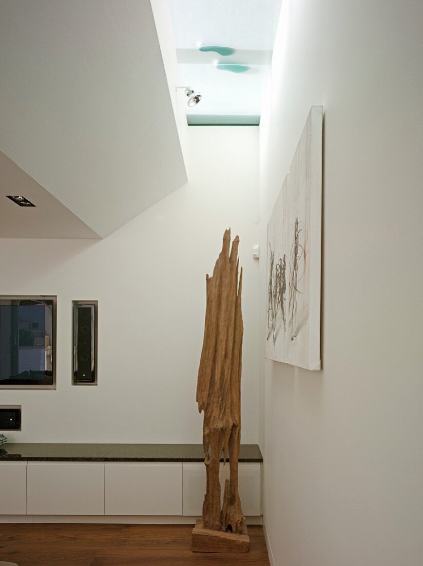 Corner of modern living room with wooden sculpture in front of low, white sideboard and narrow skylight strip
