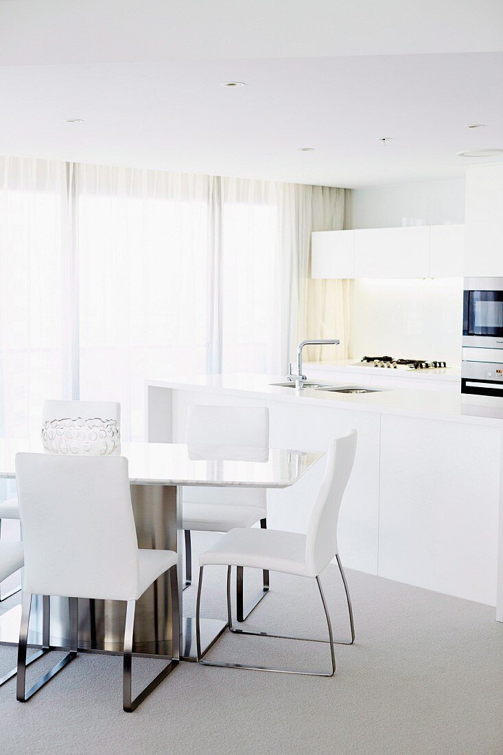 Dining table and open-plan kitchen area in white, elegant interior