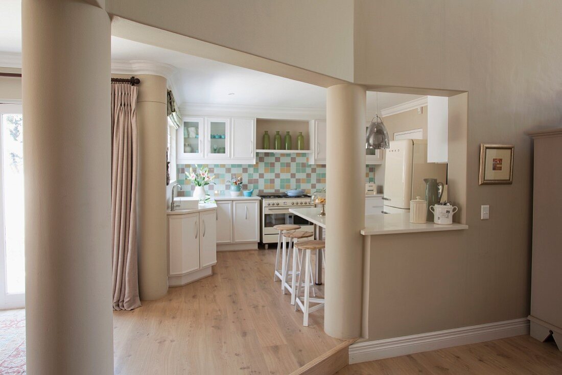 Durchgang zur Küche flankiert von Stützsäulen, weiße Einbauküche mit Mosaikfliesenrückwand, Retro-Herd, Retro-Kühlschrank & Frühstückstheke
