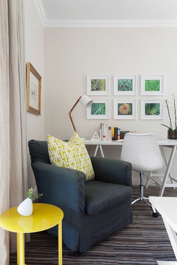 Zimmerecke mit dunkelgrauem Polstersessel & gelben Beistelltisch, dahinter Arbeitsecke mit weißem Schreibtisch & Drehstuhl