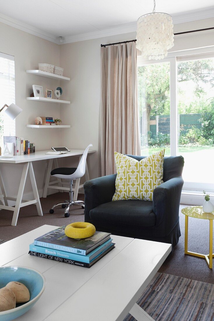 Wohnraum mit Sitzbereich aus Sessel & Sofatisch sowie Arbeitsbereich mit Schreibtisch, Bürostuhl & Regal in Zimmerecke am Fenster