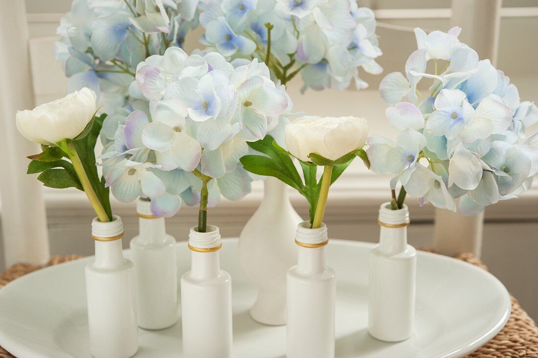 Hortensien und Ranunkeln in kleinen, weiss bemalten Flaschen und Vasen