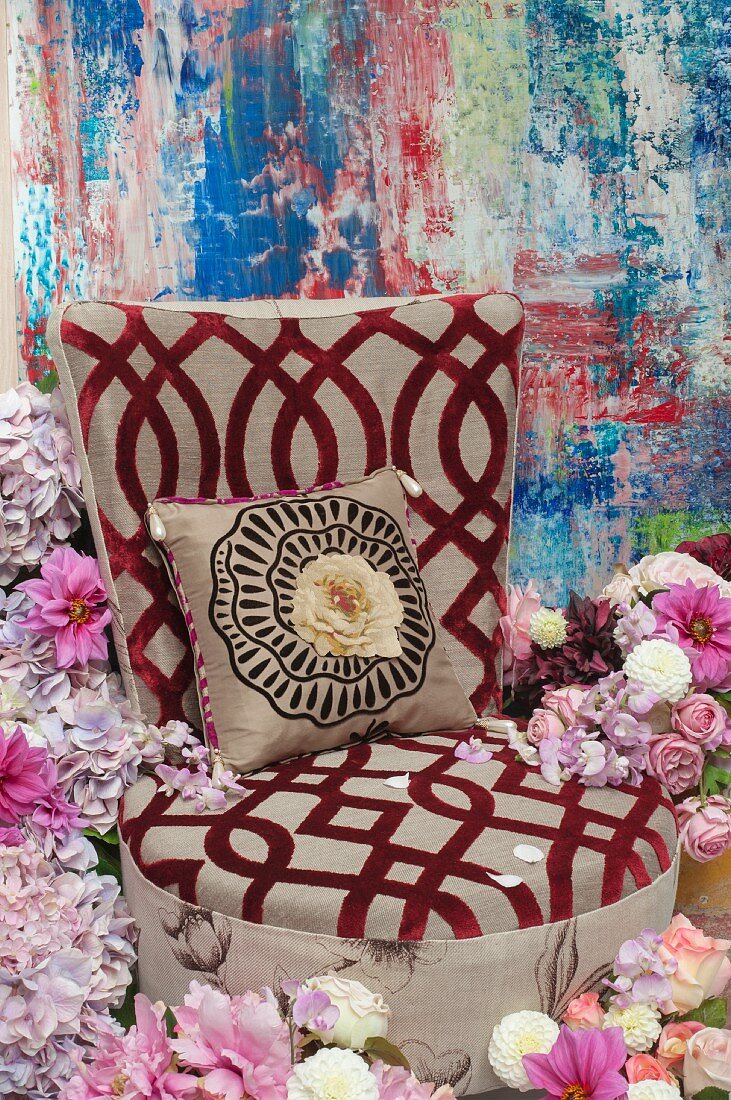 An upholstered chair with a burn-out pattern and a cushion in a sea of hydrangeas, roses and dahlias