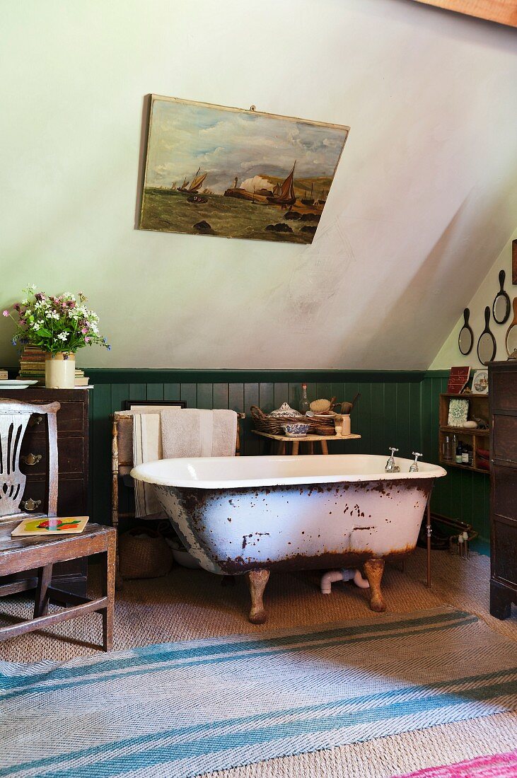 Free-standing vintage bathtub against green-painted wainscoting on sisal rug in bathroom with sloping ceiling
