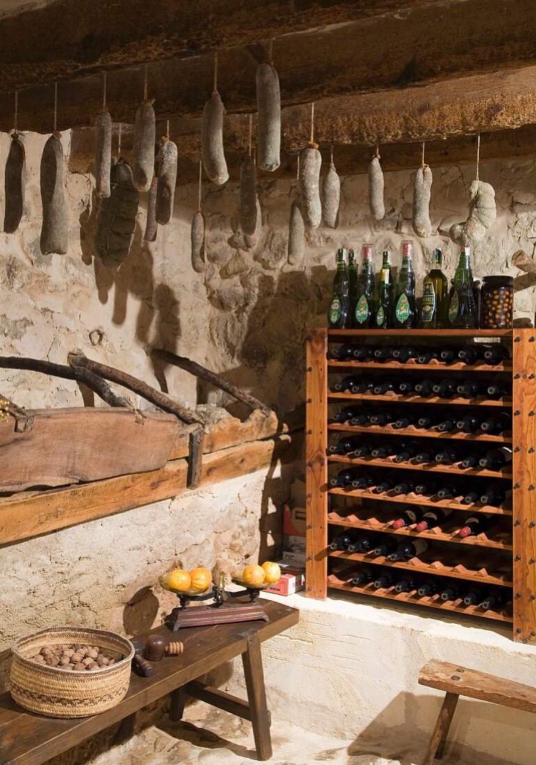 Rustikaler Vorratsraum mit Weinregalen und an Holzbalken aufgehängten Hausgemachten Würsten