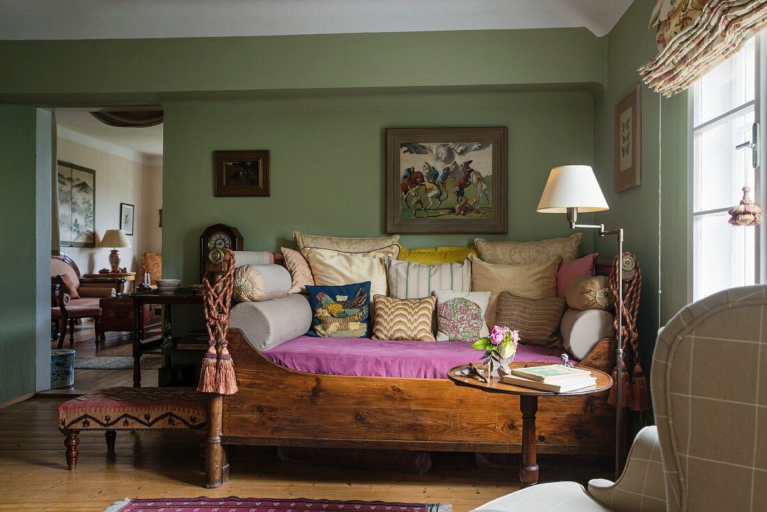Antikes Tagesbett mit Holzrahmen, viele Kissen, in grün getöntem Wohnzimmer mit traditionellem Flair