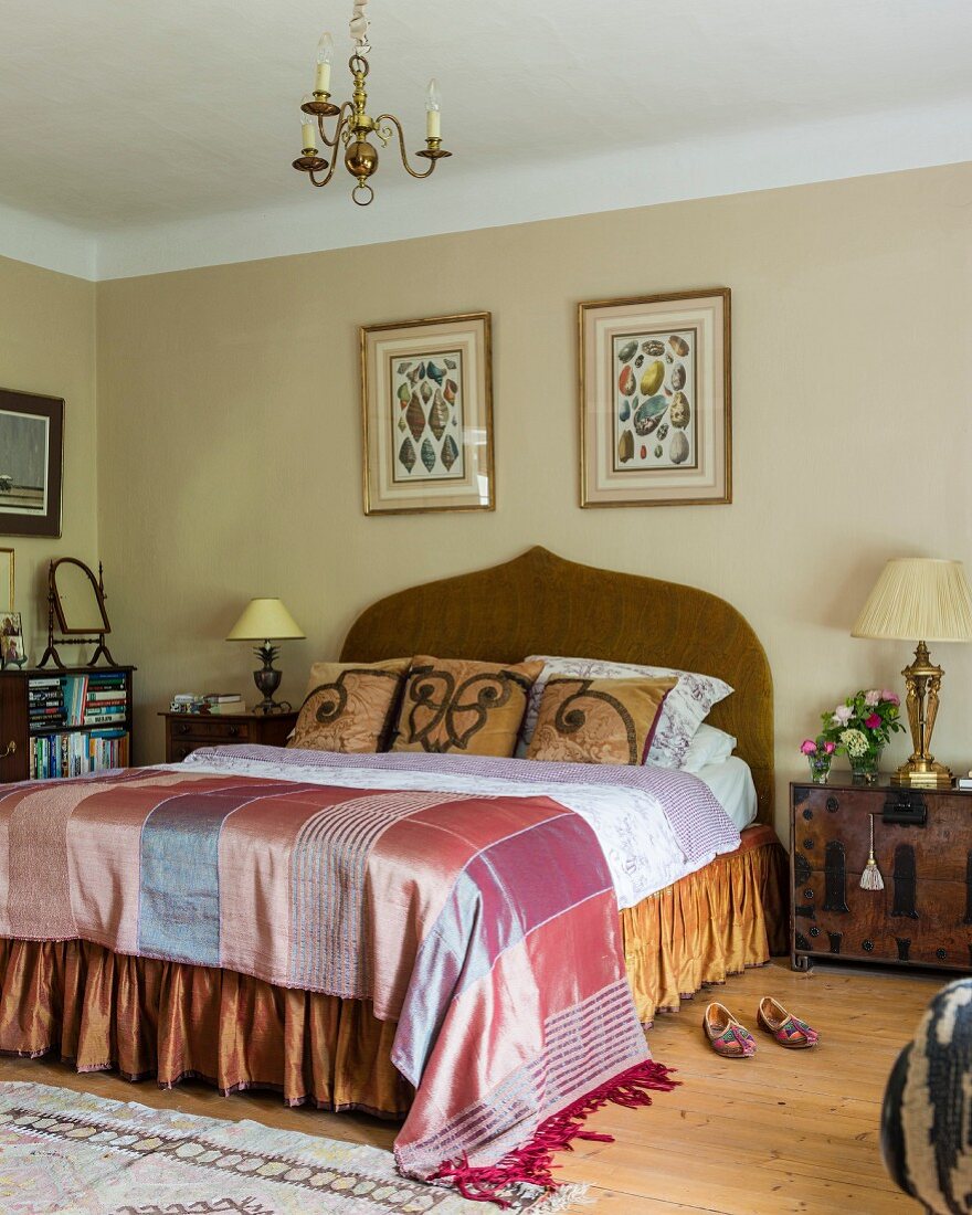 Elegant double bed with curved headboard and silk bed linen in traditional bedroom