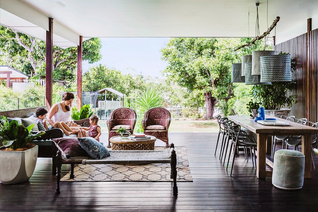 Überdachter Patio mit leichten Sitzmöbeln und Pendelleuchten über dem Esstisch, Garten im Hintergrund