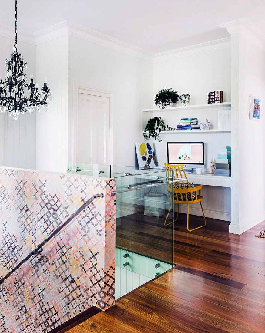 Desk and retro chair in niche, glass balustrade and staircase wall covered in wallpaper with graphic pattern