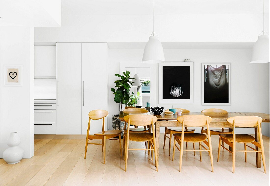 Offener Essbereich mit großem Holztisch und skandinavischen Holzstühlen vor weißen Wänden