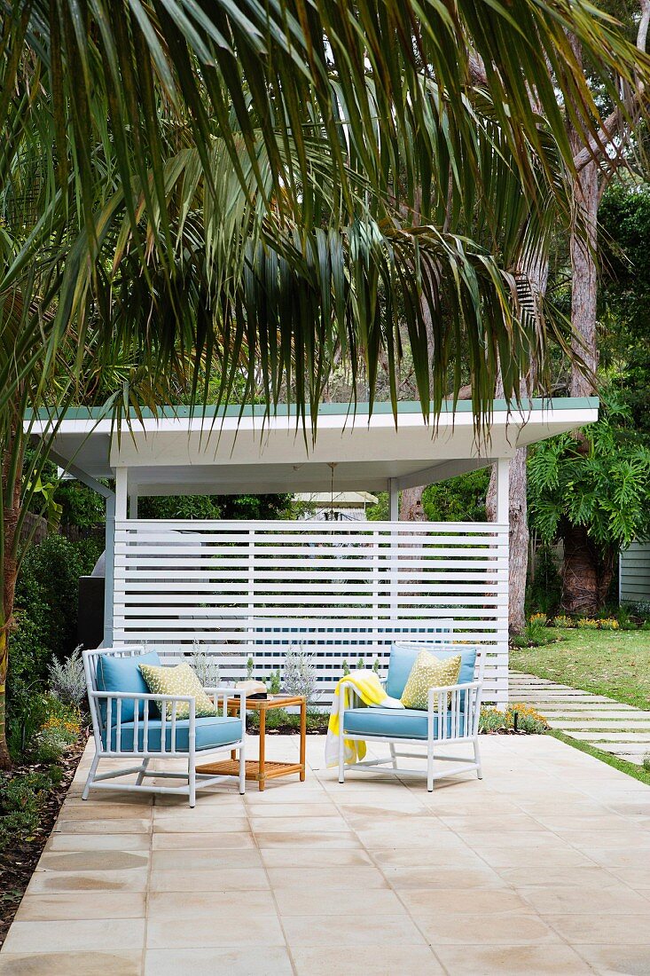 Zwei Sessel und Beistelltisch auf Terrasse im Palmengarten eines Strandhauses