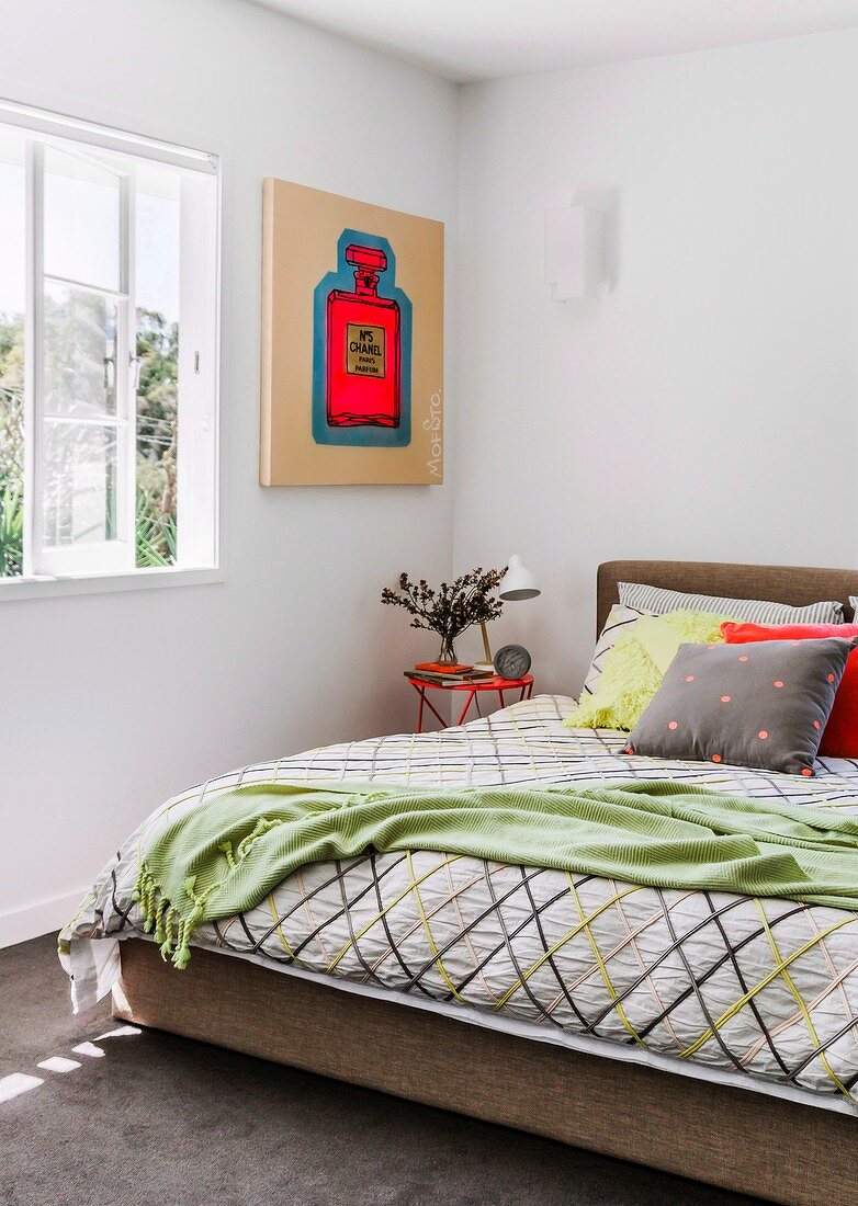 Modern artwork next to bed with graphic-patterned bedspread and scatter cushions
