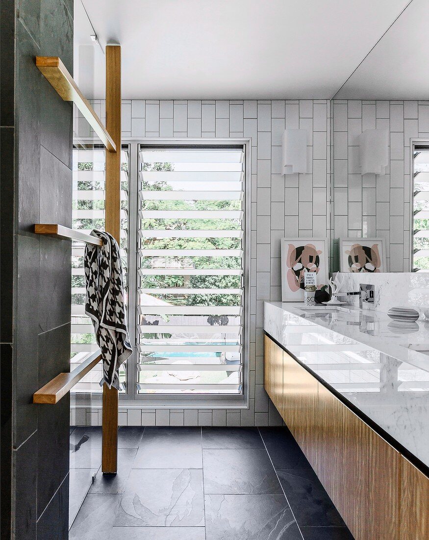 Fitted washstand and wooden towel rack in modern designer bathroom with charcoal-grey tiles