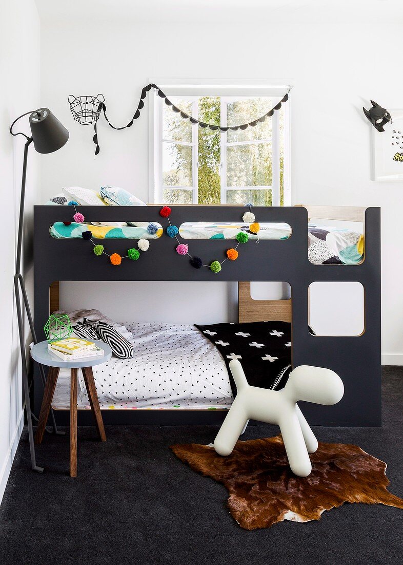Children's bedroom in charcoal grey with colourful garland of pompoms on bunk beds and dog figurine on animal-skin rug