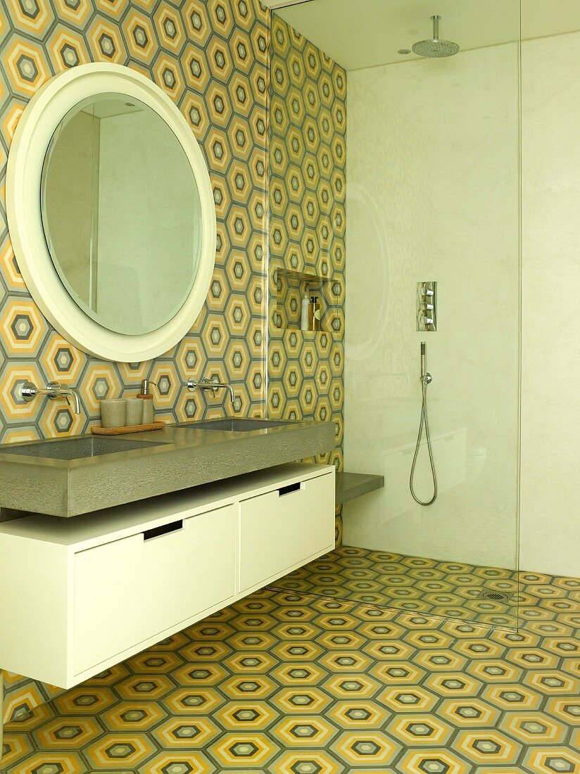 Waschtisch und runder Wandspiegel neben bodenebener Dusche mit Glas Trennscheibe im Badezimmer mit Retro Fliesen