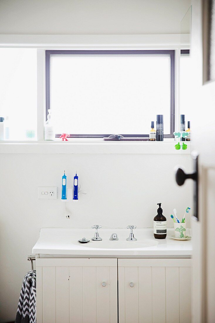 Blick durch offene Tür auf Waschtisch mit Einbaubecken in weißem Unterschrank, vor Wand mit Fensterband