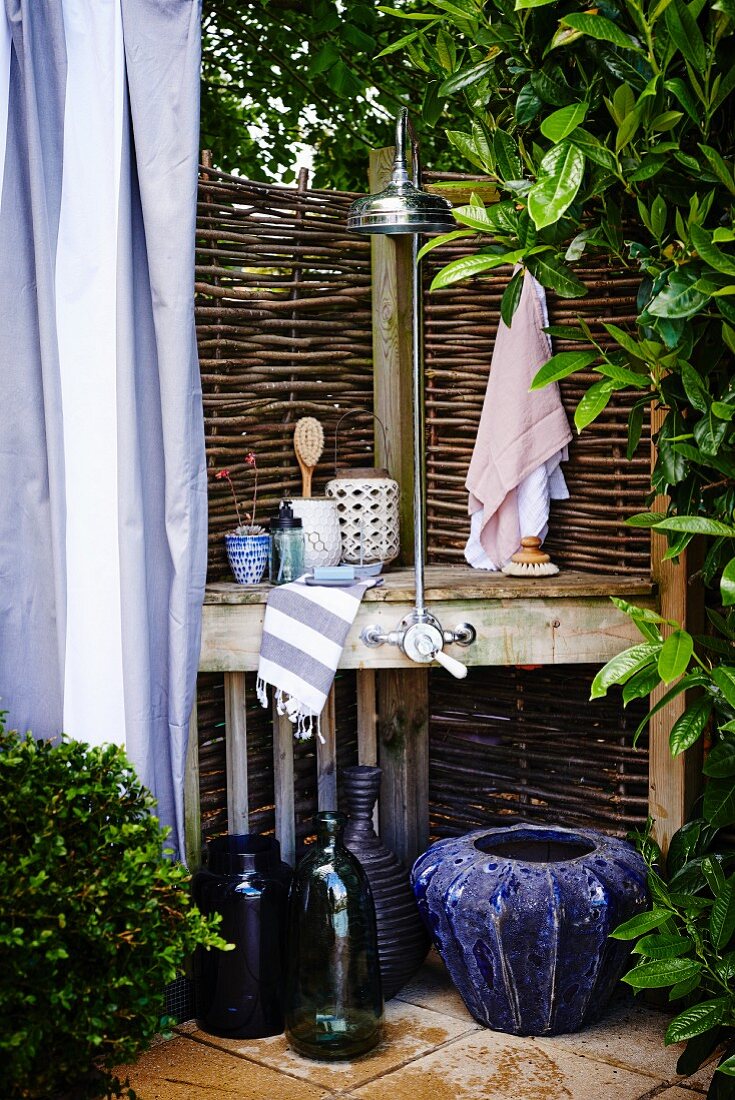 Improvisierter Duschplatz im Garten mit Sichtschutz Zaun aus Weidenzweigen, blaue Pflanzengefässe auf Boden