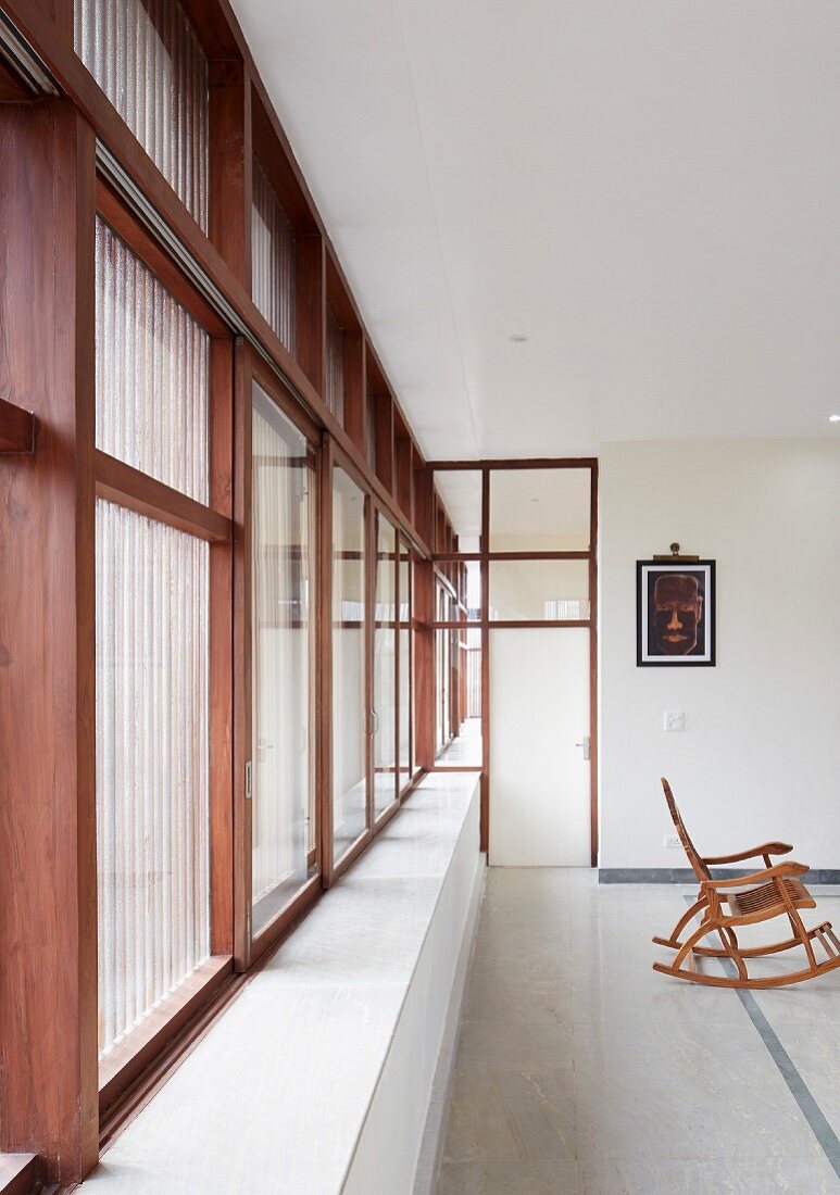 Puristischer Innenraum eines modernen, indischen Wohnhauses mit Steinboden und durchgehender Fensterfront in Holzrahmenbauweise