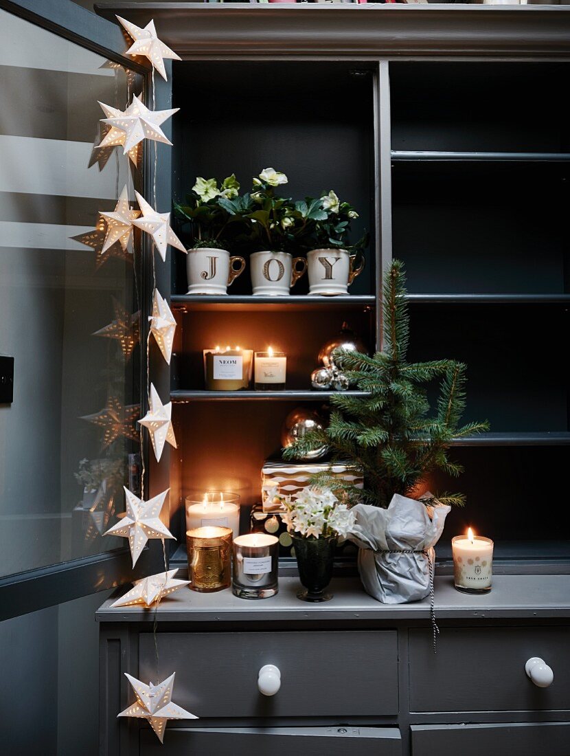 Candles, flowering plants and star-shaped fairy lights arranged on dark grey dresser