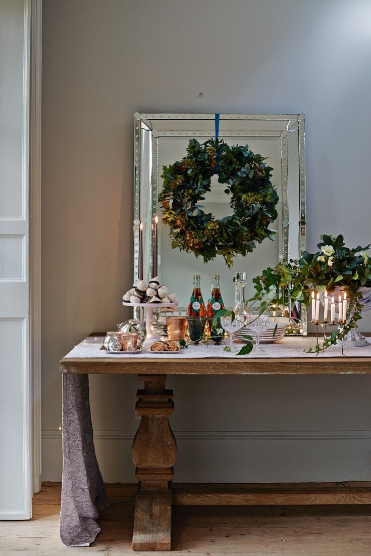 Für ein Weihnachtsbuffet festlich arrangierter Antiktisch und an Wandspiegel aufgehängter Blätterkranz