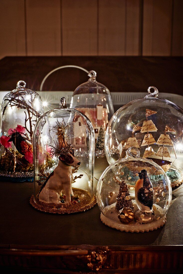 Weihnachtliche Motive und Stillleben unter kleinen Glashauben auf Antiktisch
