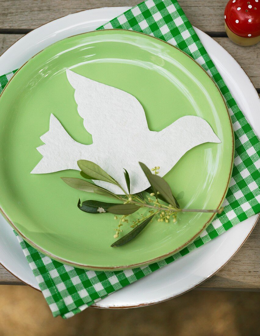 Taube aus weißem, handgeschöpftem Papier mit Olivenzweig auf grünem Teller