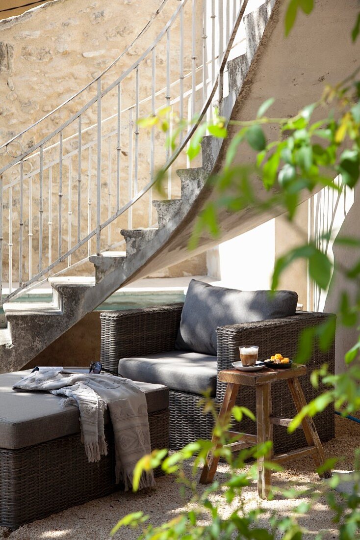 Wicker armchair with grey cushions incourtyard seating area below curved exterior staircase