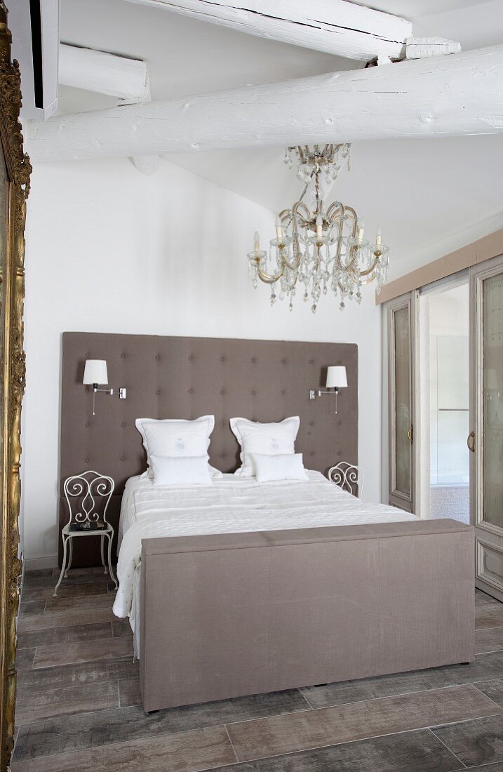 Elegant double bed with upholstered headboard below chandelier with glass ornaments
