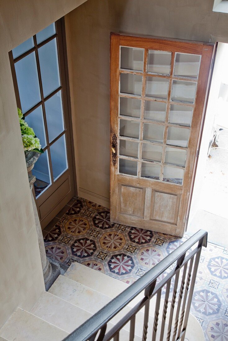 Blick von Treppe in Diele mit gemusterten Fliesenboden, offene Haustür aus abgelaugtem, hellem Holz