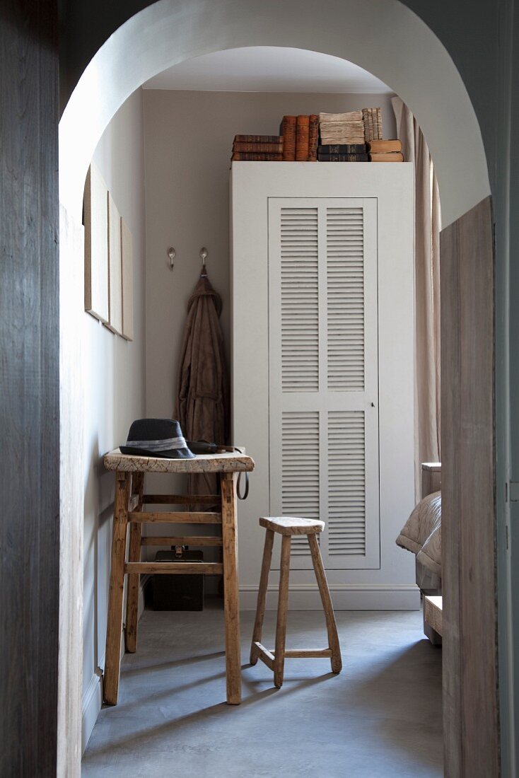 Arched doorway with view of rustic table, wooden stool and white cupboard with louver door