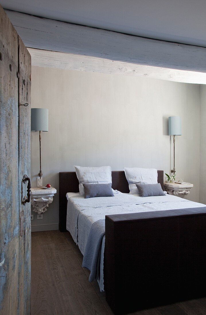 View of double bed flanked by ornate wall brackets and sconce lamps seen through open door