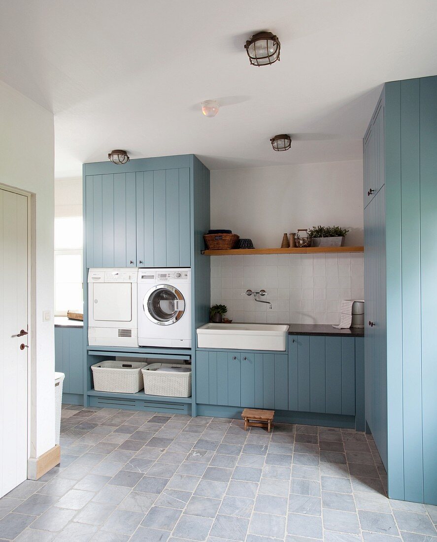 Ländliche Waschküche mit blauen Hozfronten und Steinboden