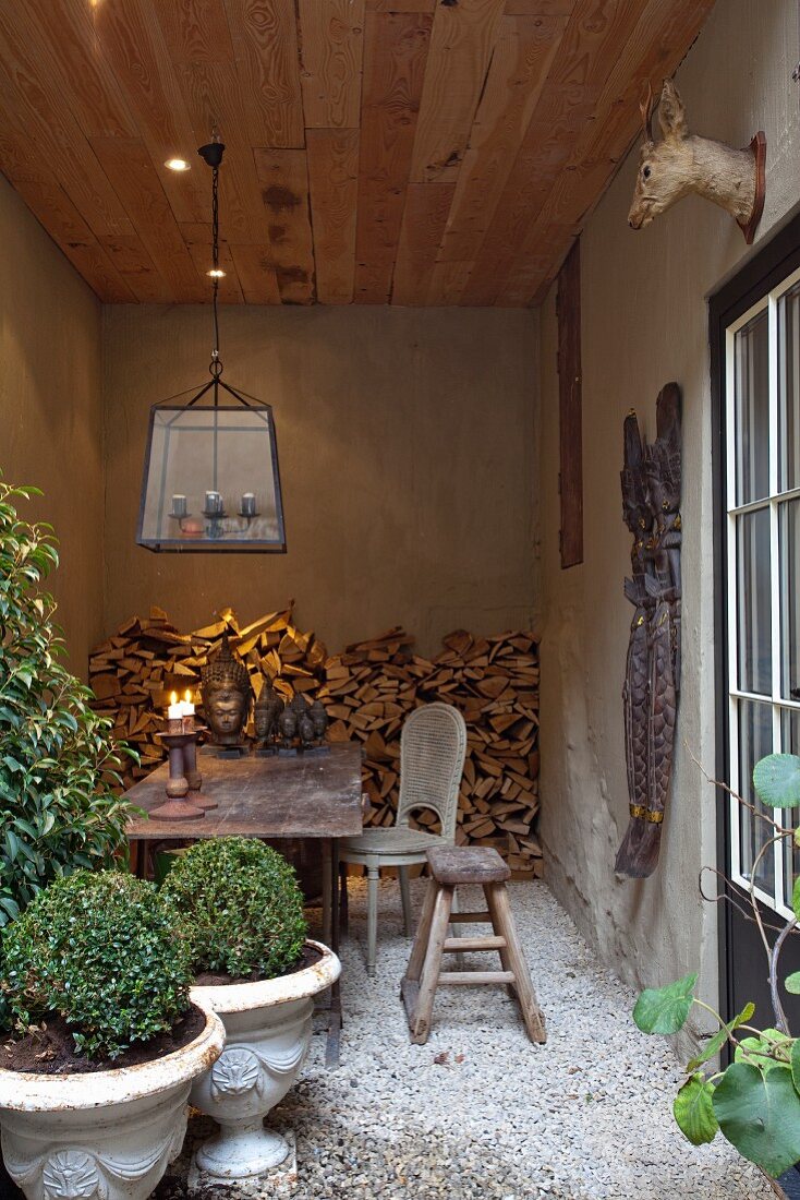 Clipped box bushed in planters and seating area in loggia with gravel floor and stacked firewood