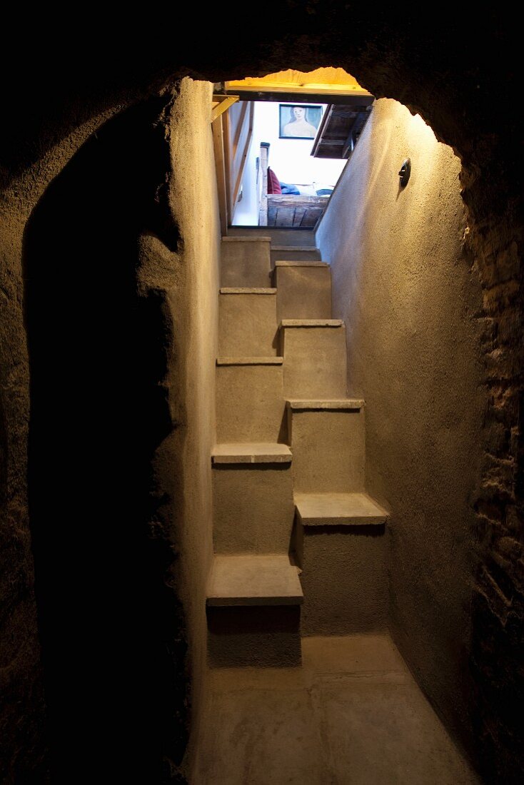 Blick durch rustikalen Rundbogen in Kellergeschoss auf betonierteSamba-Treppe
