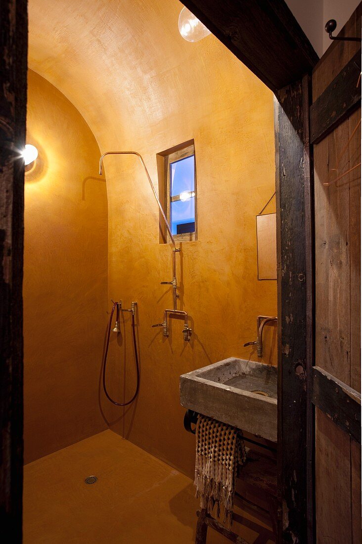 View through open door into ochre-yellow bathroom with vaulted ceiling and rustic sink