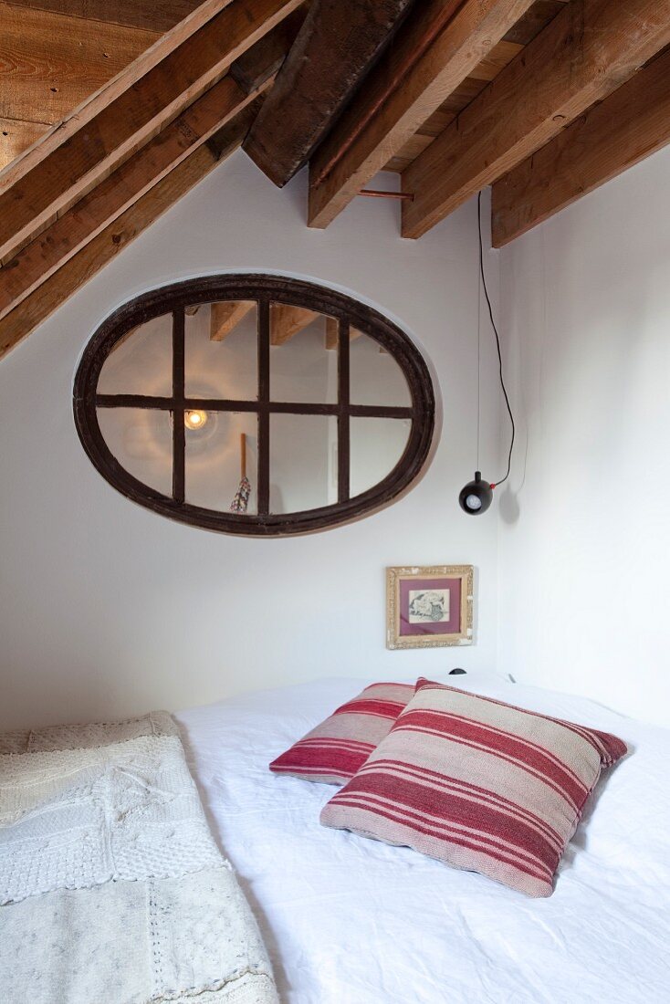 Bett in Zimmerecke unter ovalem Oberlichtfenster